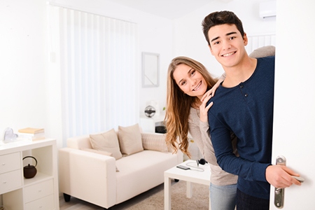happy young couple opening door and welcoming friends in apartment