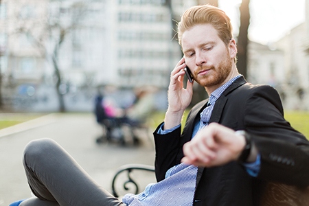 Businessman looking at his watch on a sunny day in a city park