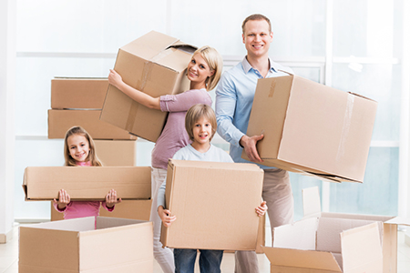 Family holding cardboard boxes and moving into a new house.