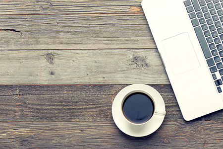 Cup of coffee and laptop on wooden table.