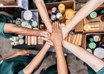 Close-up of volunteers with hands stacked during donation event outdoors