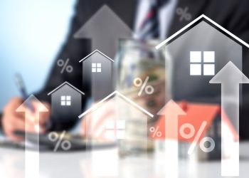 Visually striking composite image focusing on the rising cost of homeownership. Features luminous white home outlines with upward arrows and percentage signs over a blurred backdrop of a financial professional working. Perfect for representing housing market inflation, interest rate hikes, real estate investment returns, and the complexities of securing a mortgage.
