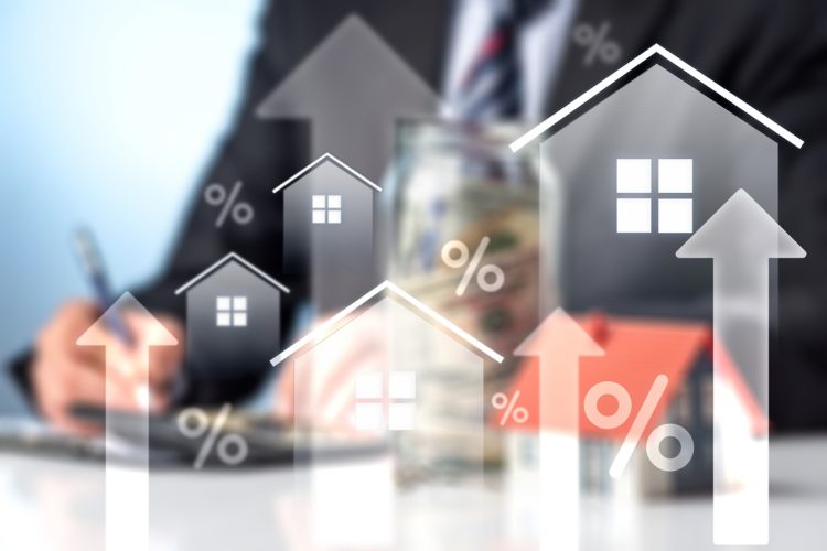 Visually striking composite image focusing on the rising cost of homeownership. Features luminous white home outlines with upward arrows and percentage signs over a blurred backdrop of a financial professional working. Perfect for representing housing market inflation, interest rate hikes, real estate investment returns, and the complexities of securing a mortgage.