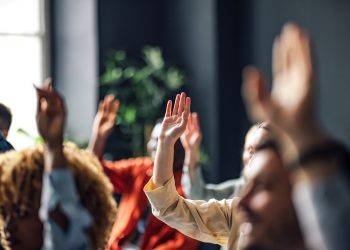 Group of people sitting on a seminar. They have their hand raised.