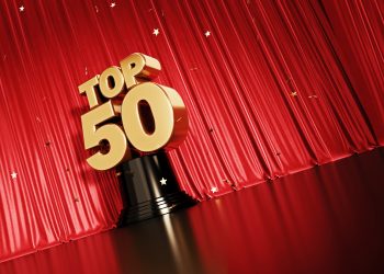 Gold colored confetti falling onto a gold top 50 award sitting before red stage curtain. Horizontal composition with copy space. Low angle view. Top 50 concept.