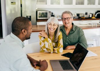 A senior couple sits with a professional, discussing life insurance options. They review documents, focusing on structuring life cover within their financial plan, including ownership, beneficiaries, premiums, and coverage to ensure it meets their long-term needs.