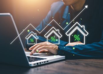 Businessman working on laptop with digital house icons and rising percentage graph, representing real estate investment, property market growth, mortgage rates, and housing finance.