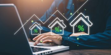 Businessman working on laptop with digital house icons and rising percentage graph, representing real estate investment, property market growth, mortgage rates, and housing finance.