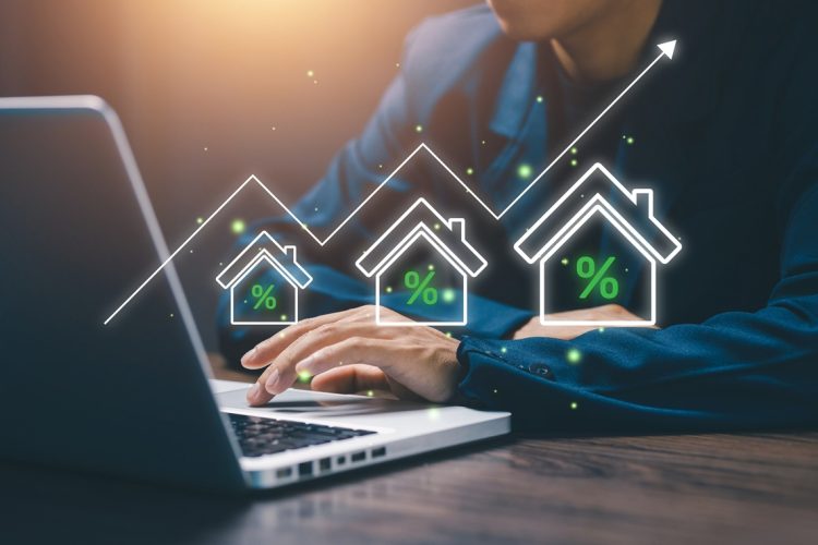 Businessman working on laptop with digital house icons and rising percentage graph, representing real estate investment, property market growth, mortgage rates, and housing finance.